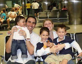 Family smiling on airport benches, holding snacks and bags while waiting in a terminal