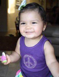 Smiling child in a purple tank top holding a colorful toy indoors