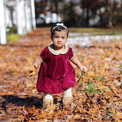Toddler in a burgundy dress walking through fallen autumn leaves outdoors
