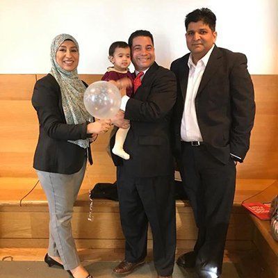 Four people posing on a stage, one holding a child and a clear balloon.