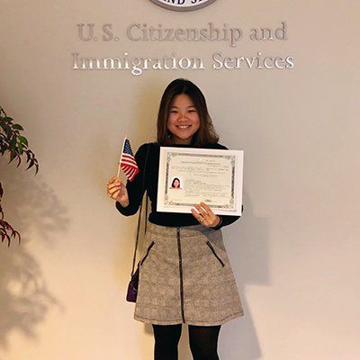 Woman holding a certificate and small U.S. flag at a U.S. Citizenship and Immigration Services ceremony