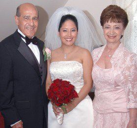 Wedding portrait of three people, with the bride in a white dress holding red flowers and two guests beside her