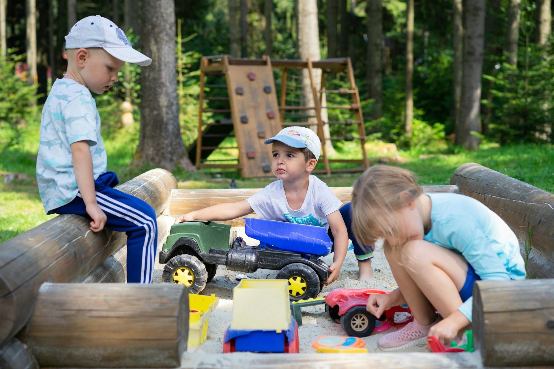 Children playing with toy trucks in a sandbox at a park.