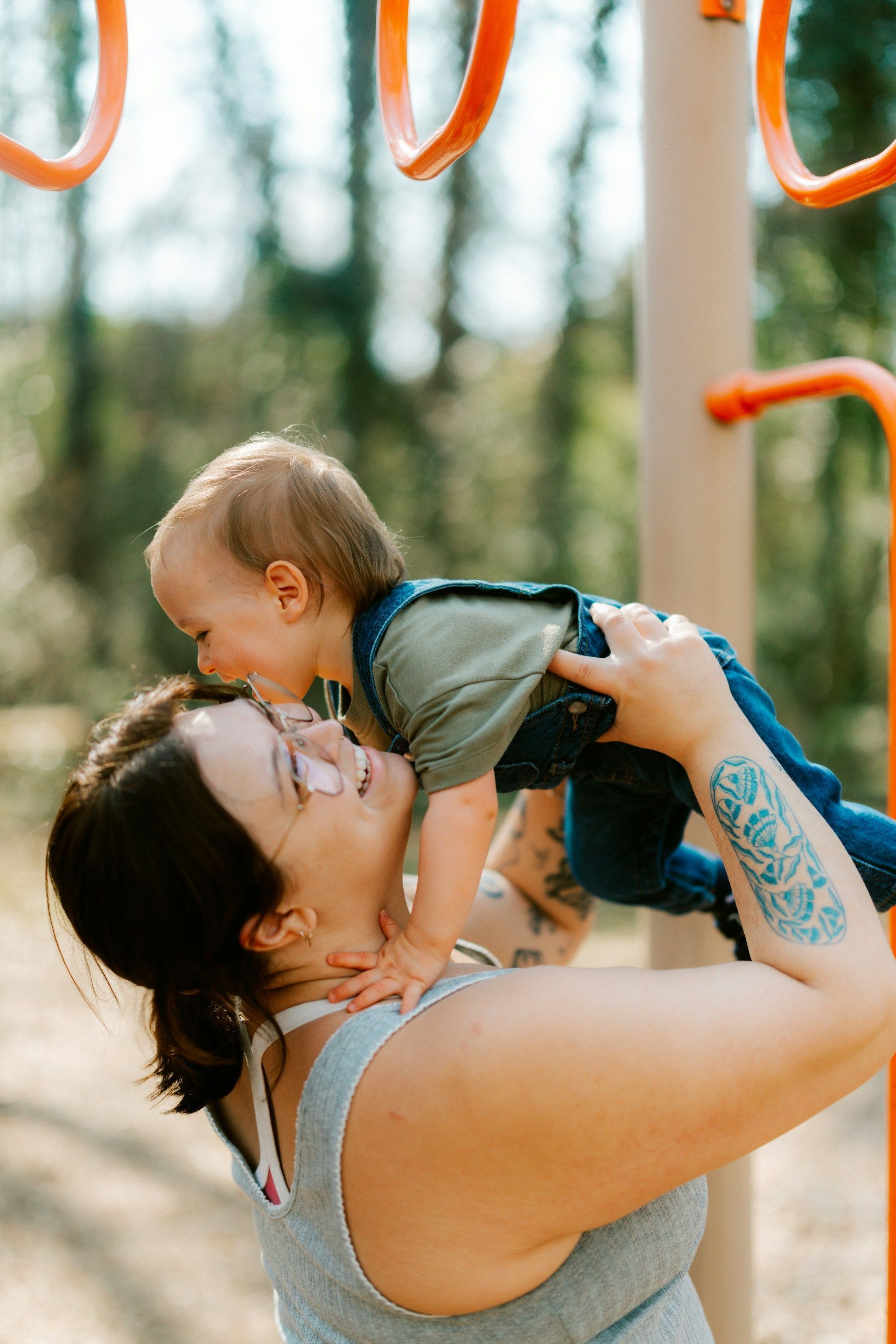 Woman lifting and kissing a baby outdoors near playground bars