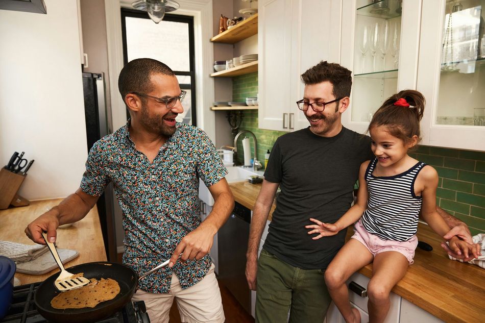 Three people cooking and talking in a bright kitchen, with a child sitting on the counter.