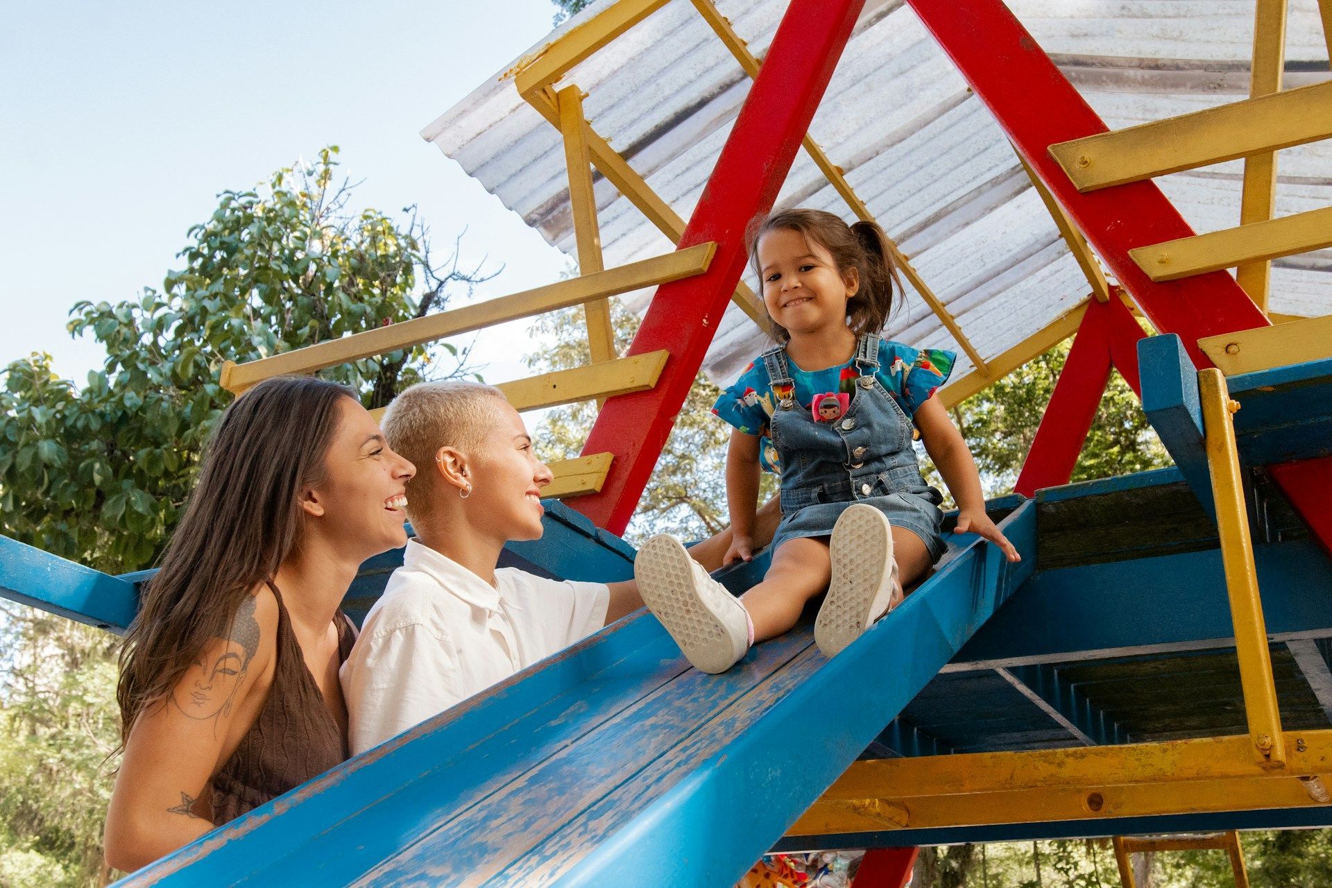Three people smiling on a colorful playground slide under a bright sky