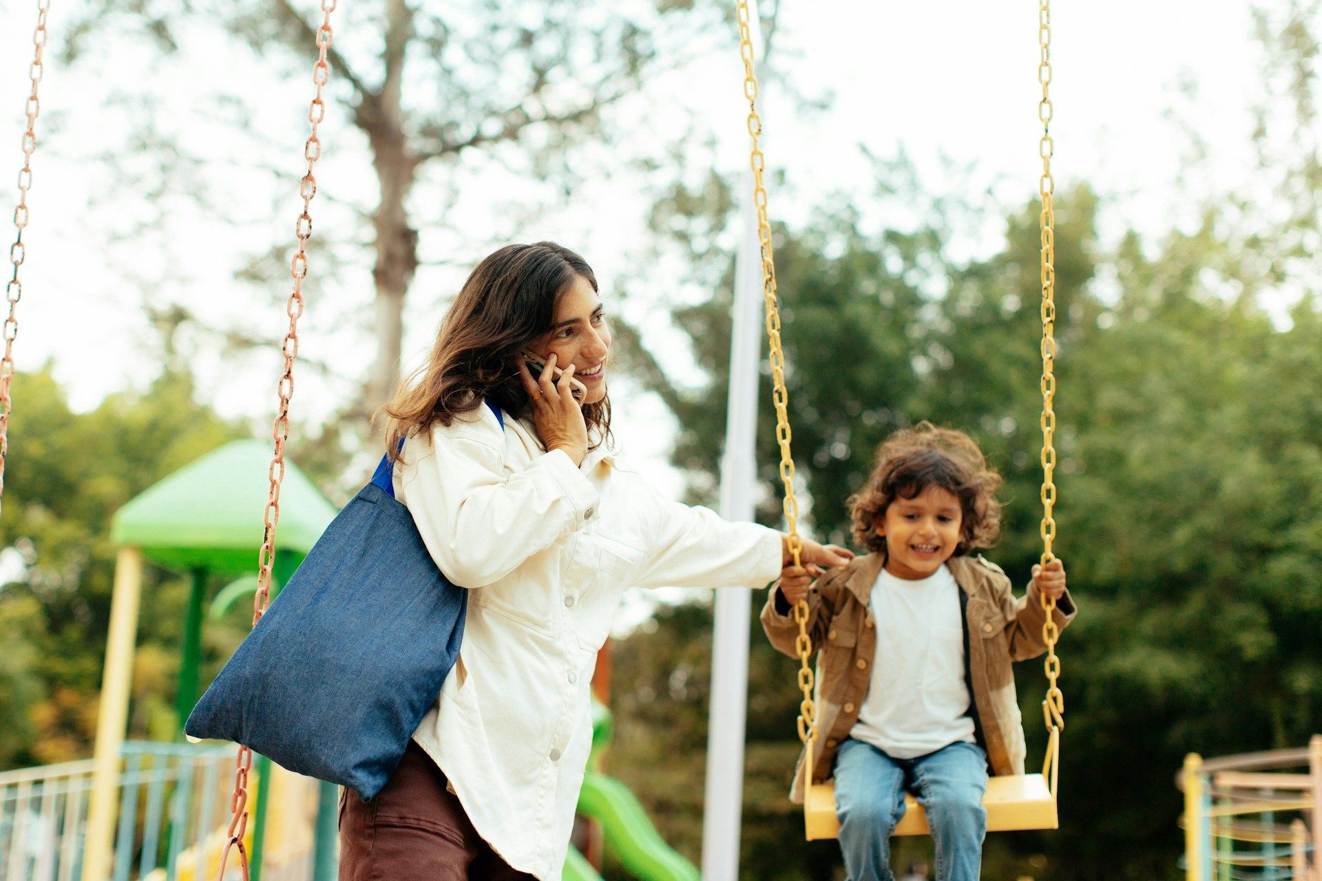 Adult helping child on a swing in a sunny park
