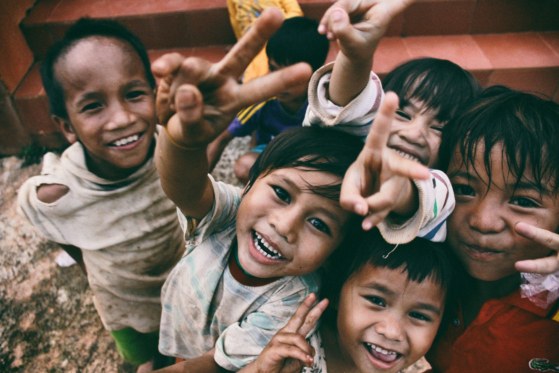 Smiling children reaching toward the camera in a colorful outdoor group selfie