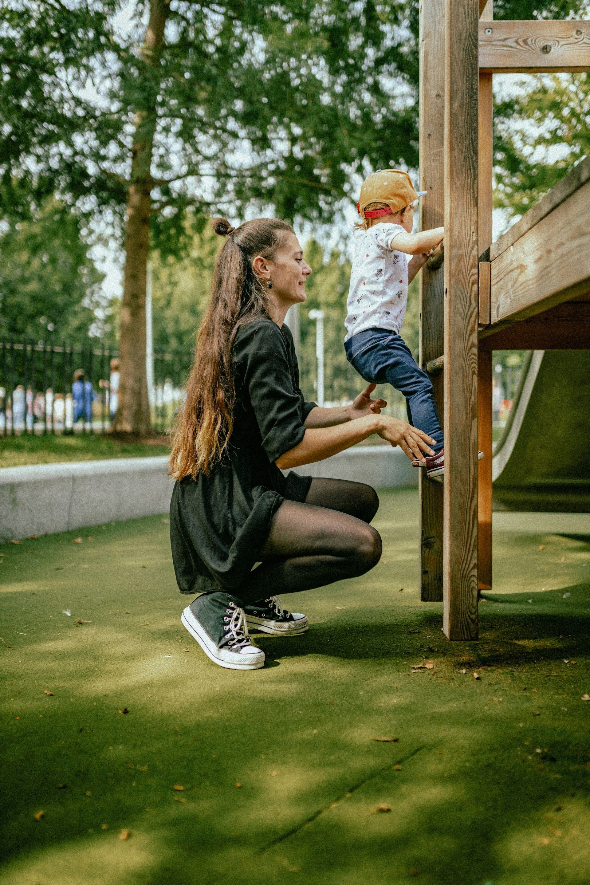 Adult helping child climb a wooden play structure in a park