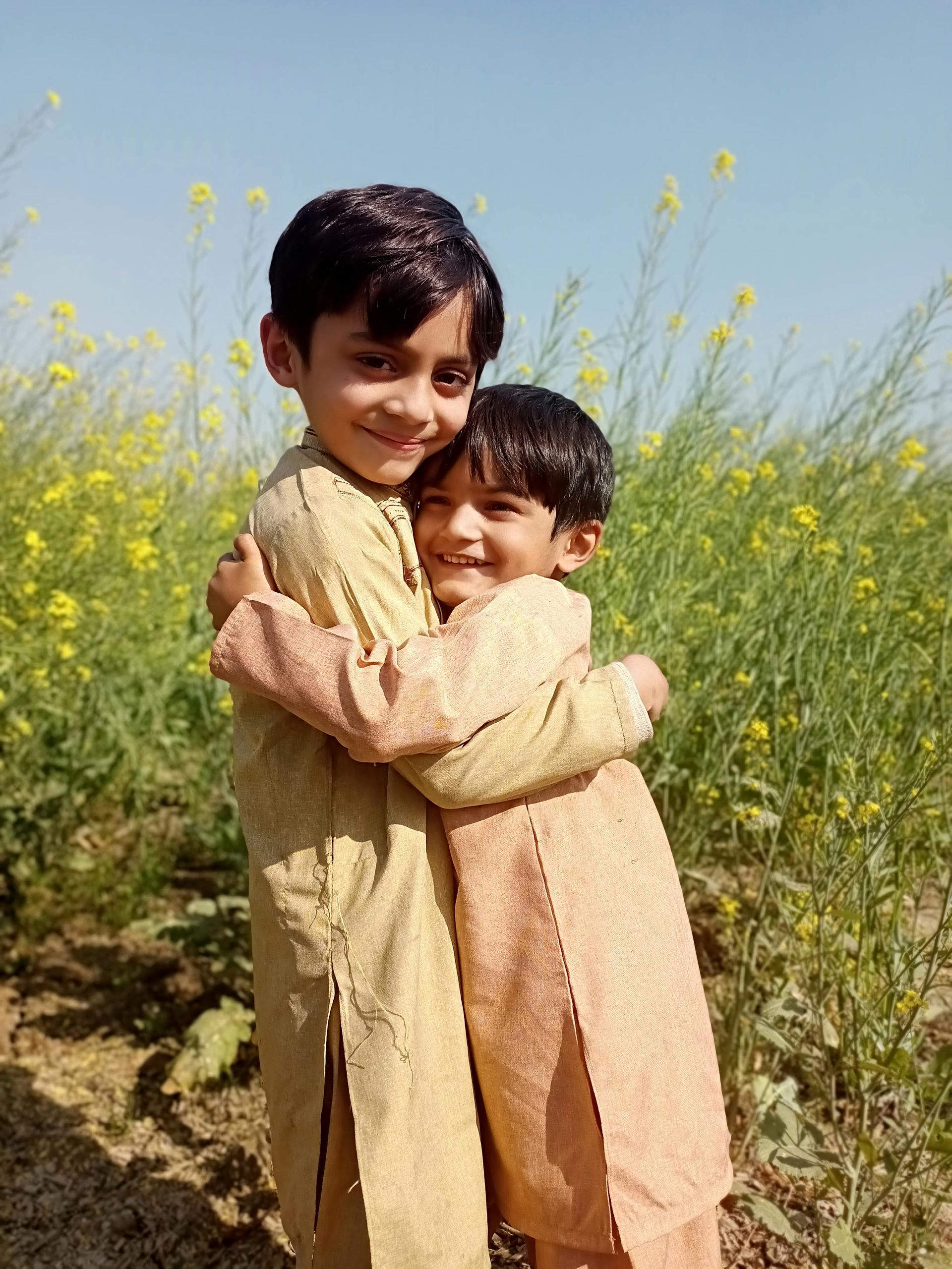 Two children hugging in a yellow flower field on a sunny day.