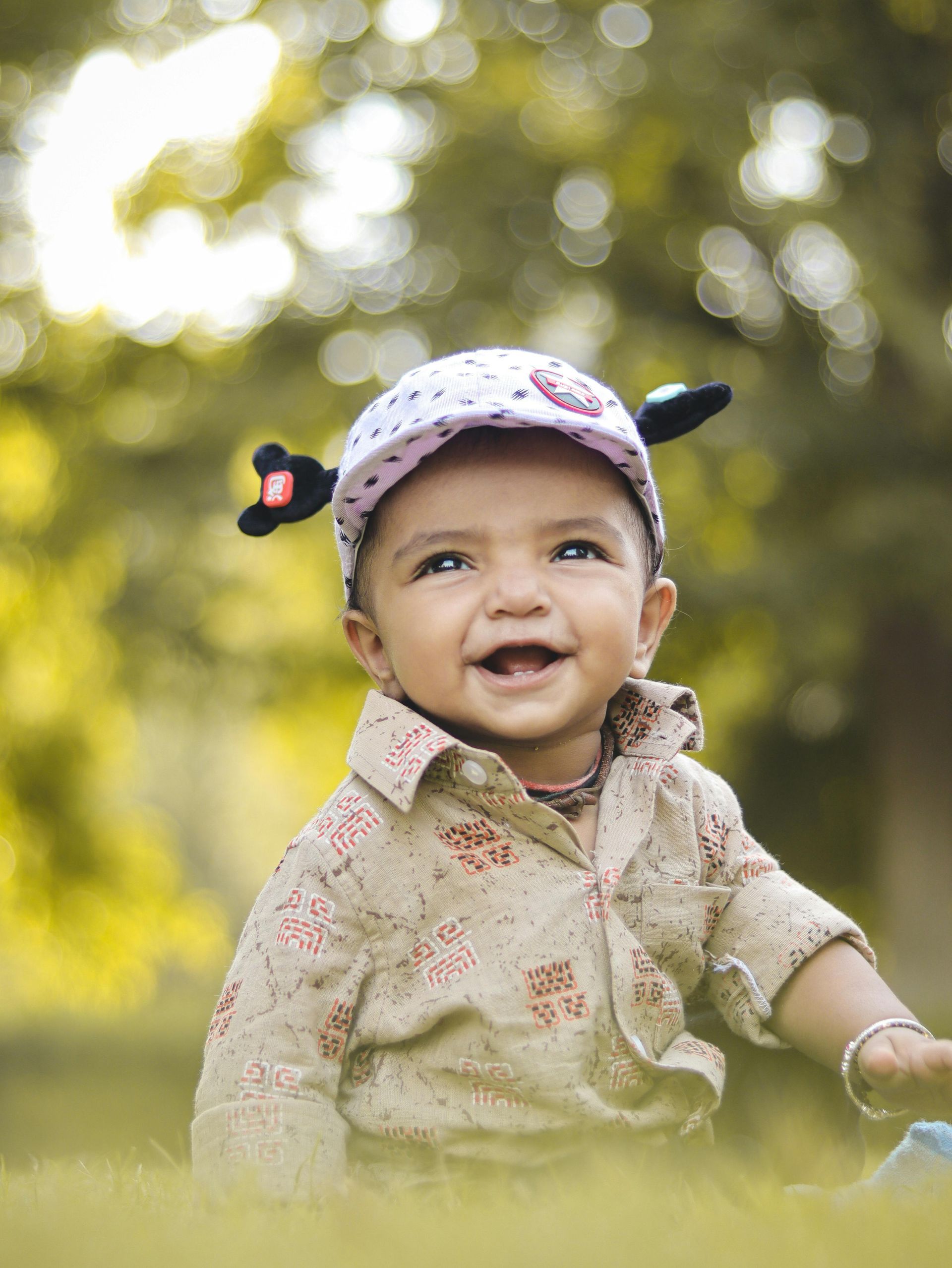 Smiling baby in a floral cap walking through a sunlit grassy field