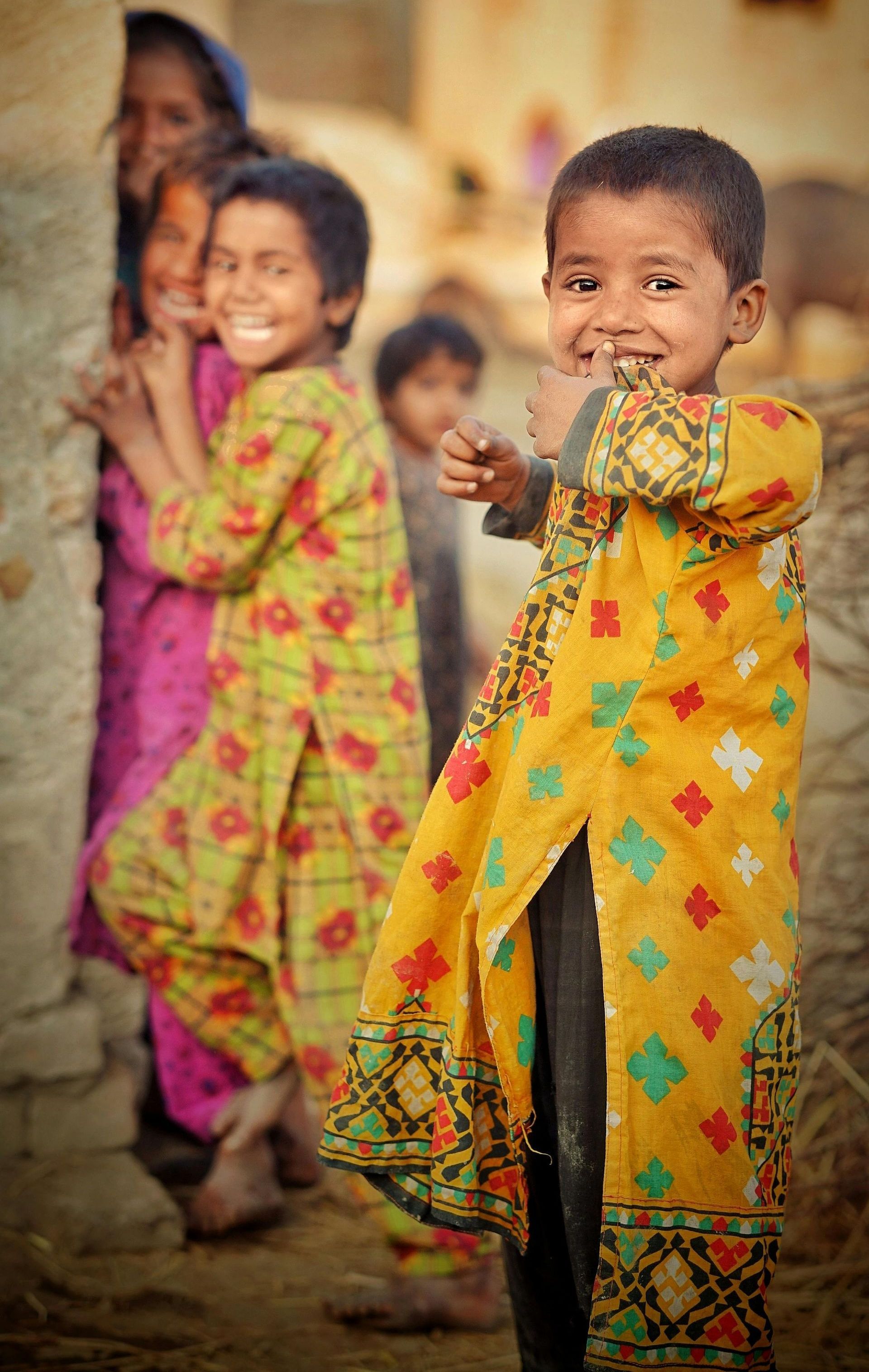 Children in bright patterned clothes standing outdoors, one child smiling at the camera.