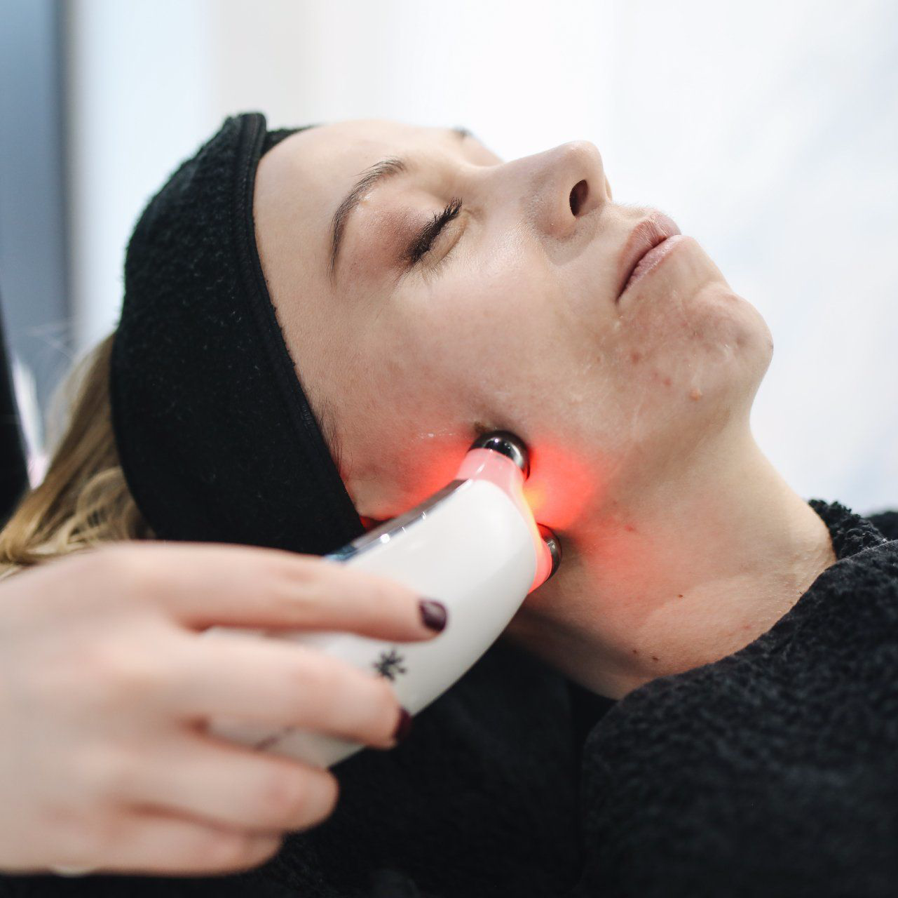 Frau erhält Gesichtsbehandlung mit einem von der Hand gehaltenen Rotlichttherapiegerät.