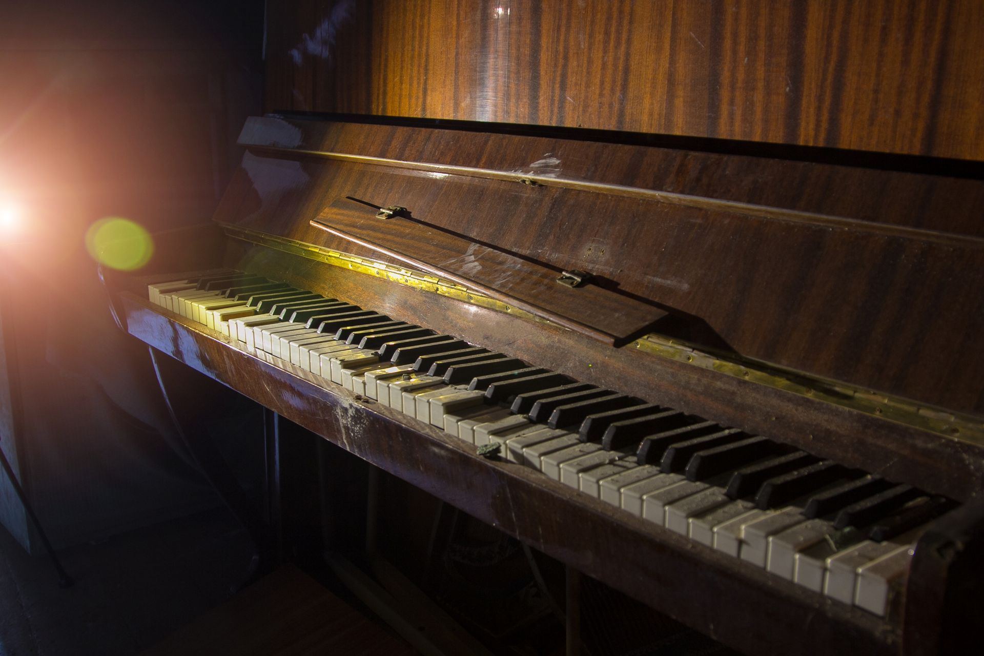 Old, dusty piano with broken keys in a dim room; light flare.