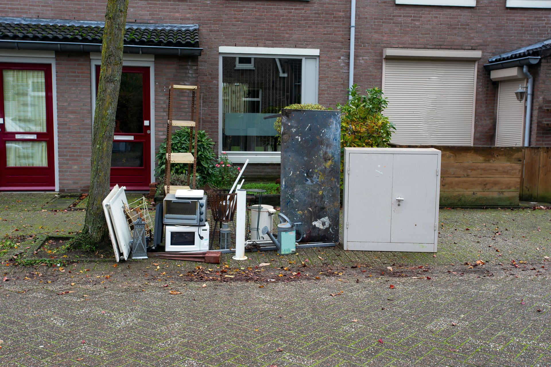 Discarded furniture and appliances piled on a curb in front of a brick building.