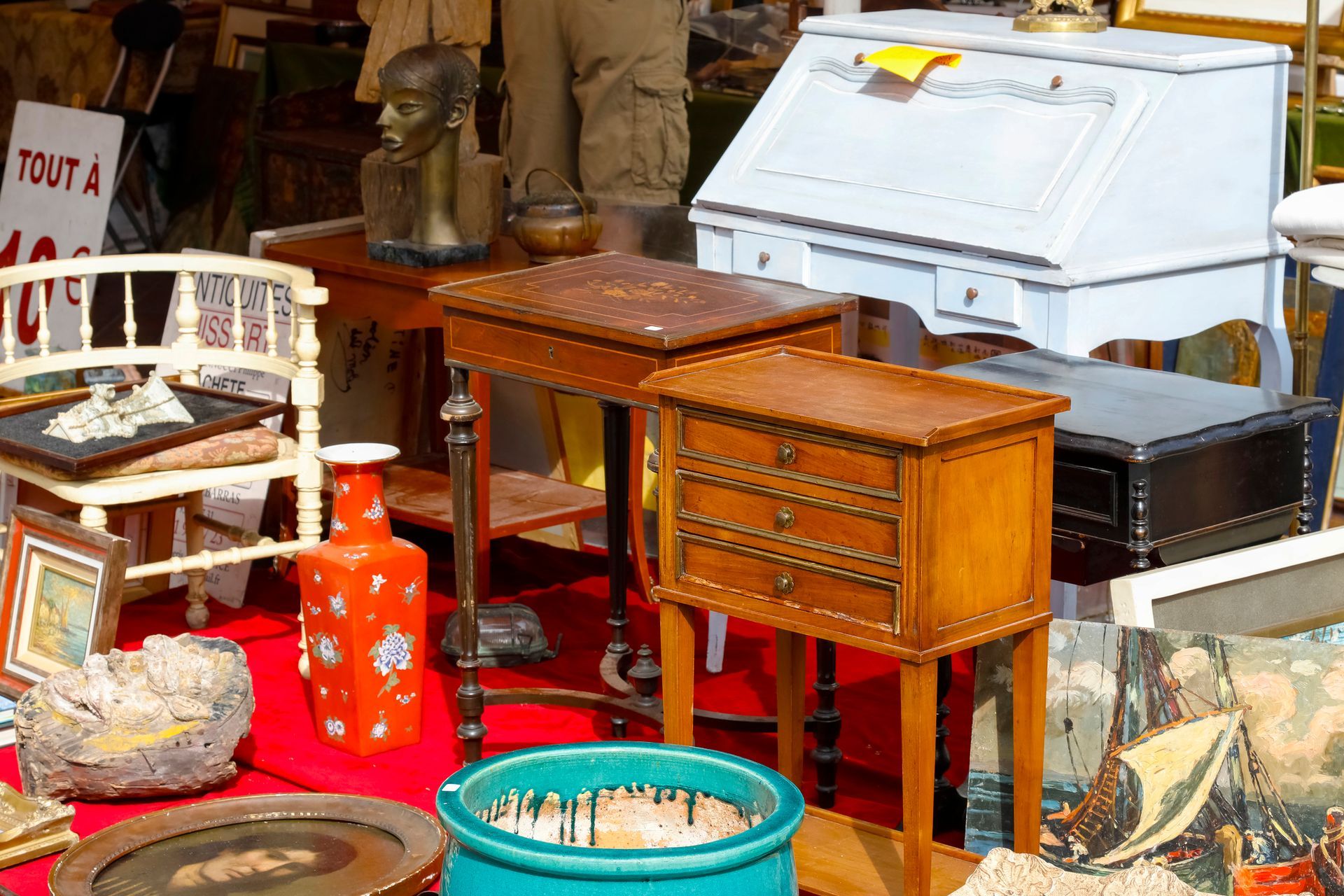 Flea market display of assorted furniture and decor, including a desk, tables, and a statue.