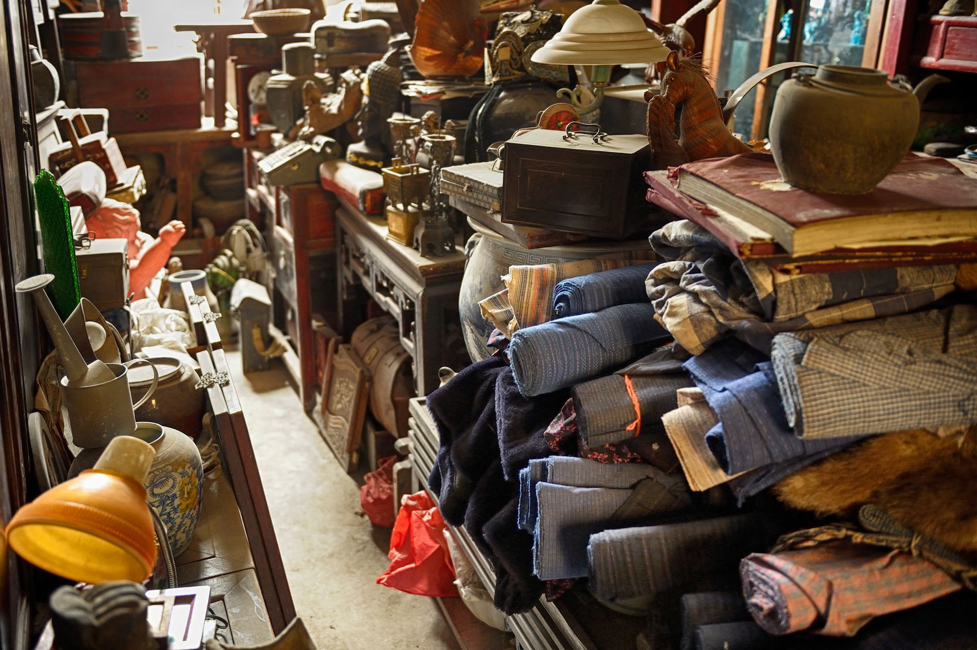 Cluttered antique shop interior: Various objects on shelves and tables, tight space, dim lighting.