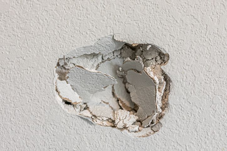 Hole in a white textured wall, exposing damaged plaster.
