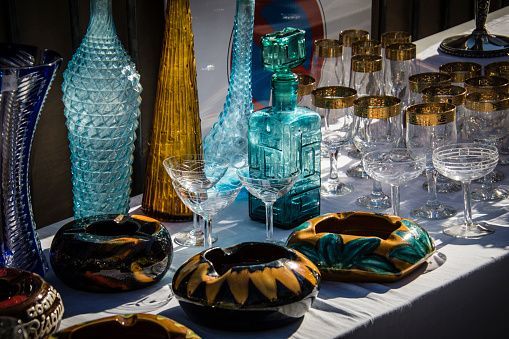 Collection of colorful glass bottles, glasses, and ashtrays on a white tablecloth.