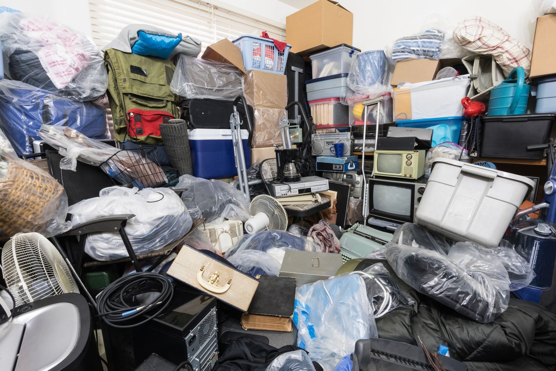 Cluttered room, overflowing with boxes, electronics, and various items; a chaotic storage space.