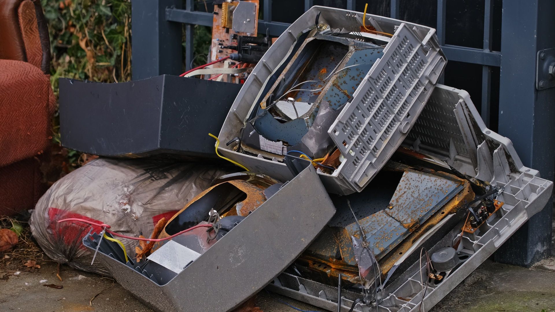 Pile of broken electronic devices, including monitors, next to a fence.
