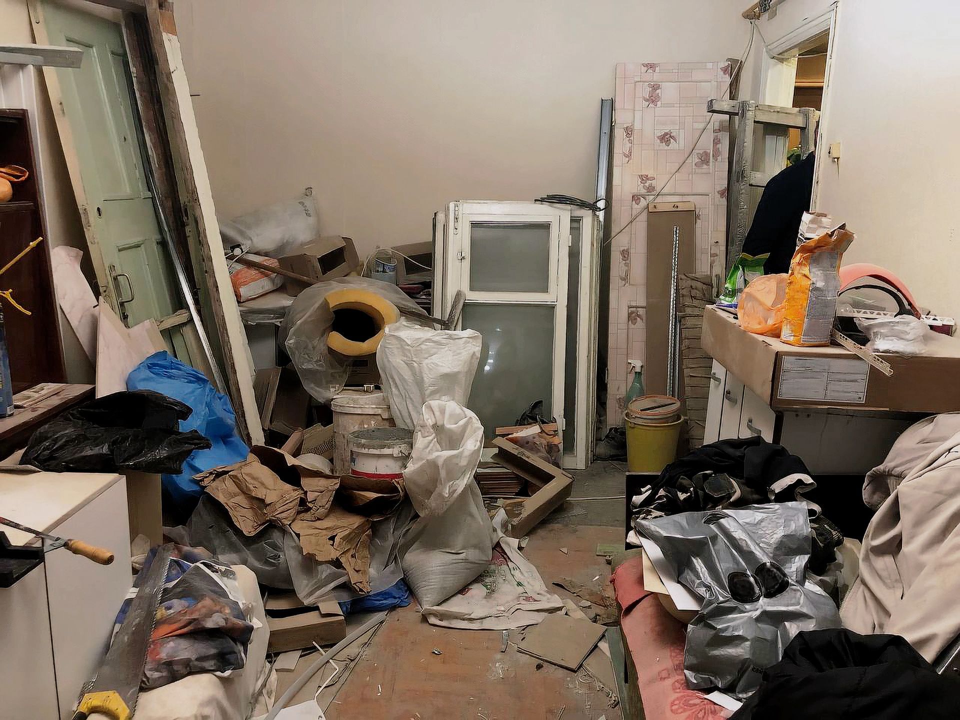 Cluttered room with various construction materials, boxes, and debris scattered around.