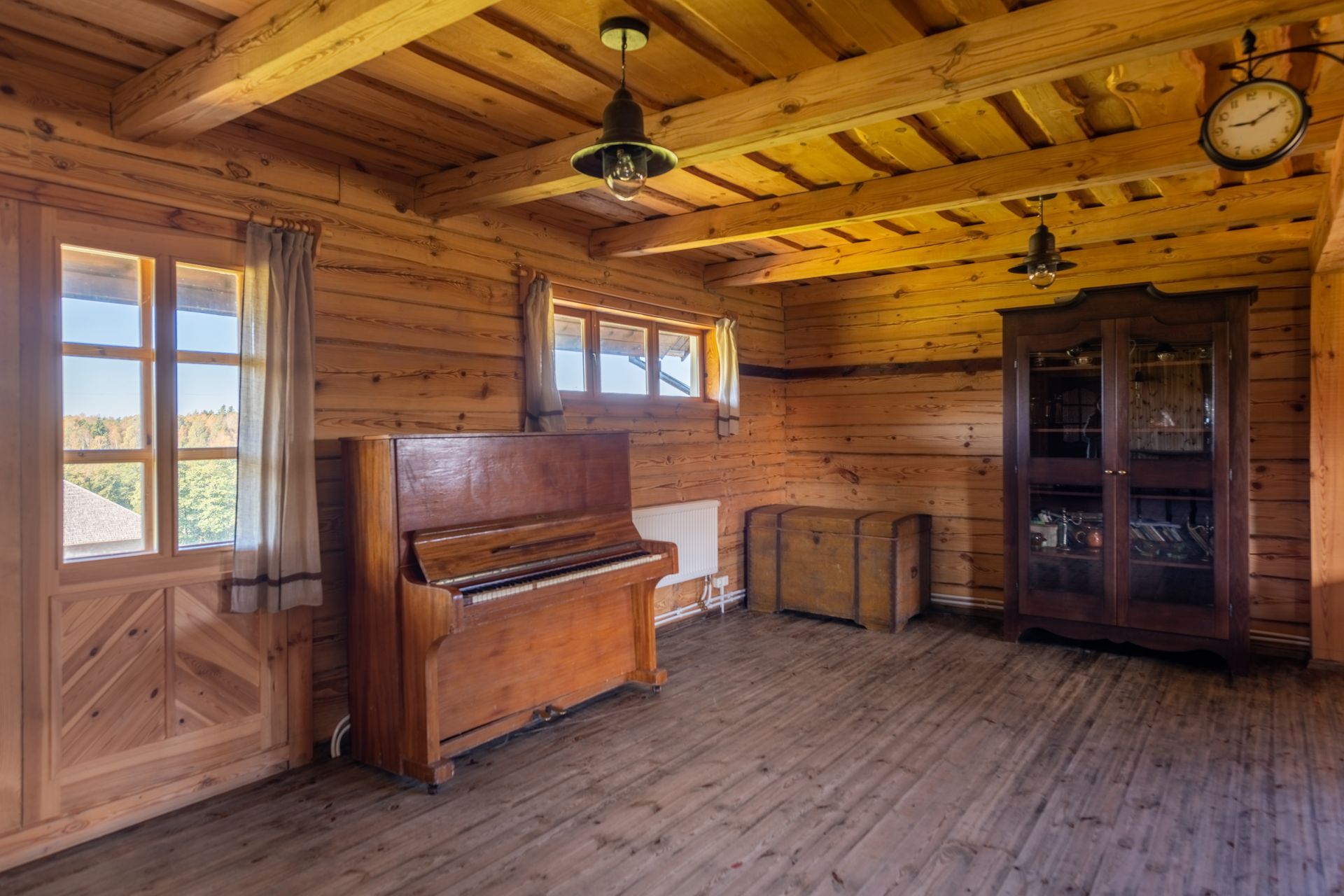 Wooden interior: piano, cabinet, clock, and windows in a sunlit log cabin.