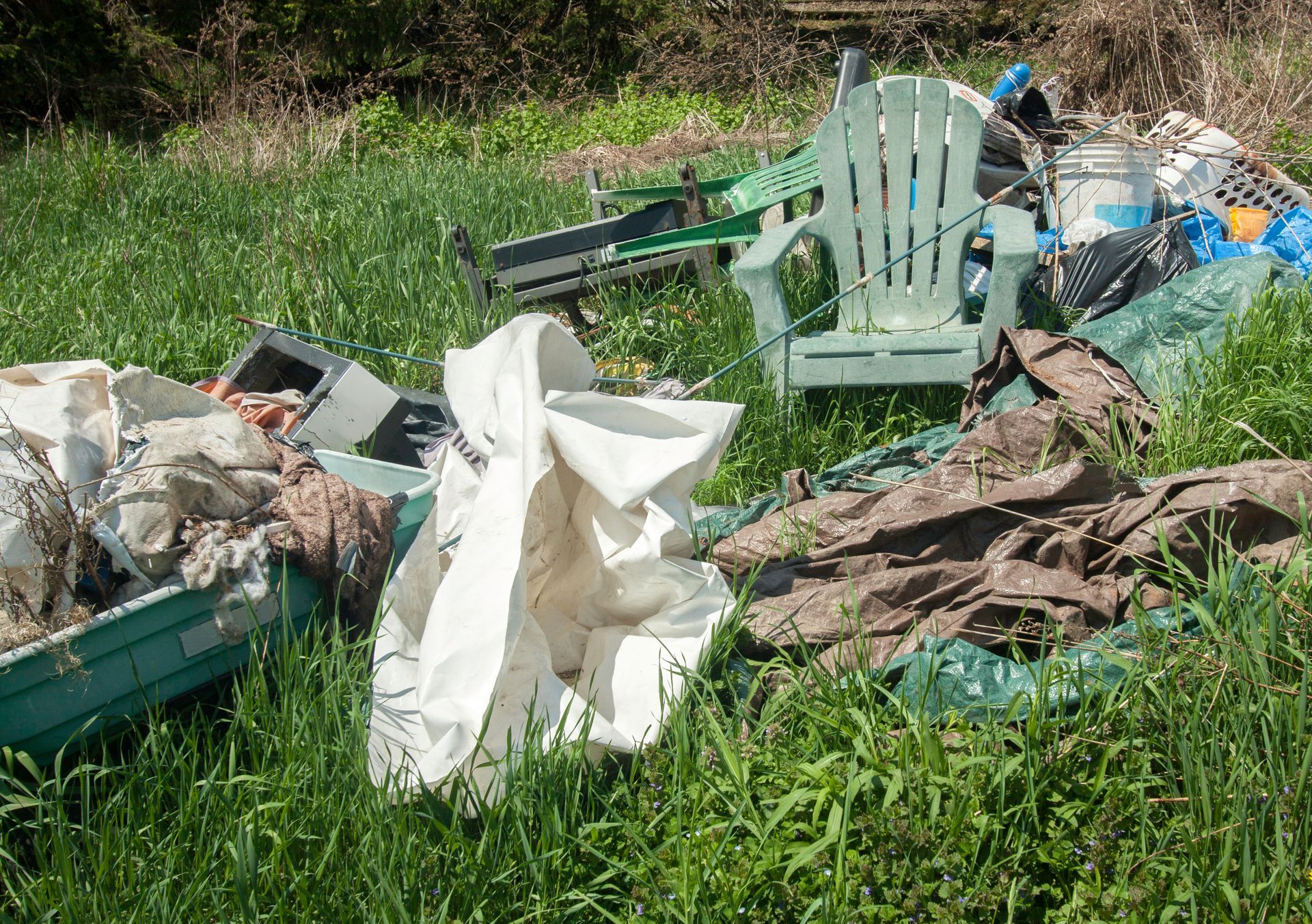 Pile of trash in grassy field, including a green chair, plastic containers, and debris.