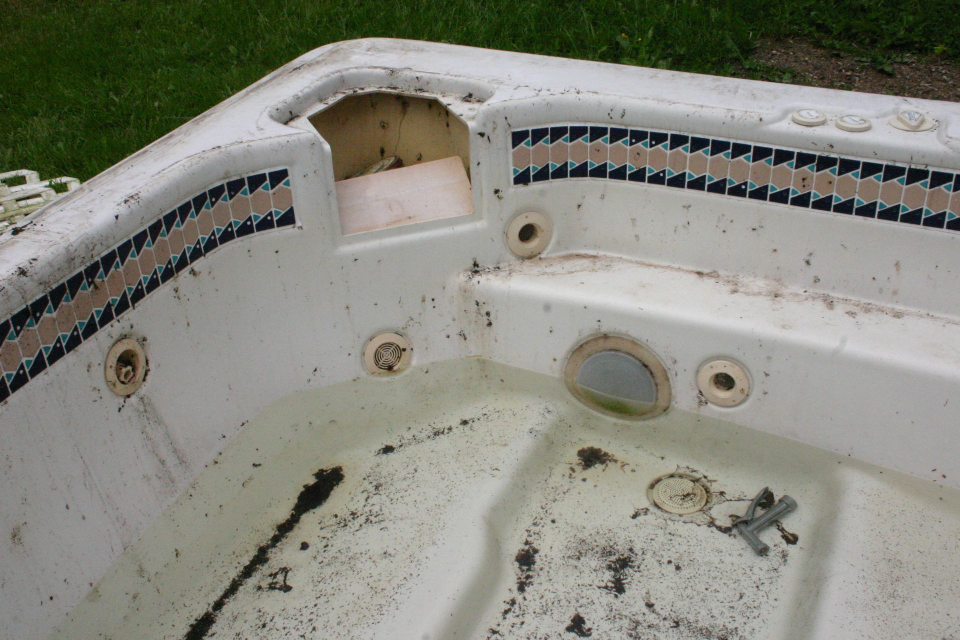 Dirty, abandoned hot tub with missing parts. Features blue and tan tile trim, and a small step.