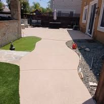 Curved concrete patio path beside a house, bordered by grass, gravel, and a small red planter.