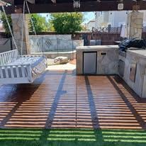 Covered patio with white bench, outdoor counter, and slatted sunlight casting striped shadows on the floor.