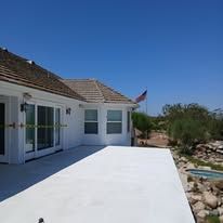 White house patio with sliding doors, blue sky, and a small American flag by a rocky garden.