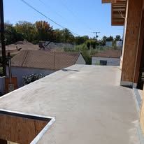Flat rooftop patio beside a house, overlooking neighboring roofs under a clear blue sky