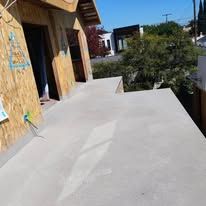 Concrete patio beside a house under construction, with plywood-covered walls and trees in the background