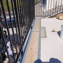 Balcony with black railing, white floor, blue wall, and a parked car visible below.