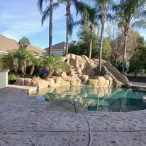 Backyard pool with rock waterfall, palm trees, and patio in a sunny suburban setting