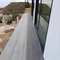 Modern house balcony with gray decking and floor-to-ceiling glass overlooking a hillside.