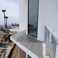 Balcony with glass door overlooking a rocky seaside pool and palm trees