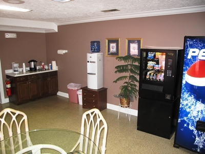 Office break room with coffee station, white refrigerator, vending machines, and tables and chairs