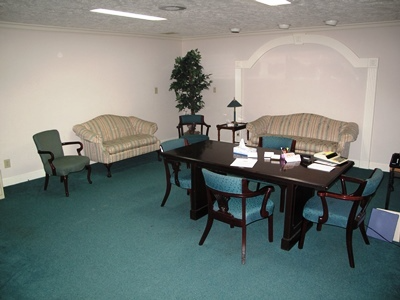 Office lounge with dark wood table, chairs, sofas, and a potted tree on green carpeted floor