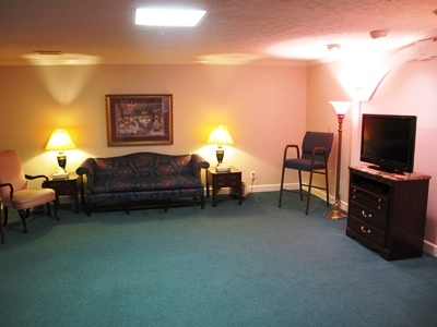 Empty living room with teal carpet, sofa, lamps, chairs, and a TV on a dresser