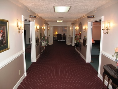 Hotel hallway with maroon carpet, beige walls, wall sconces, and open doors on both sides.