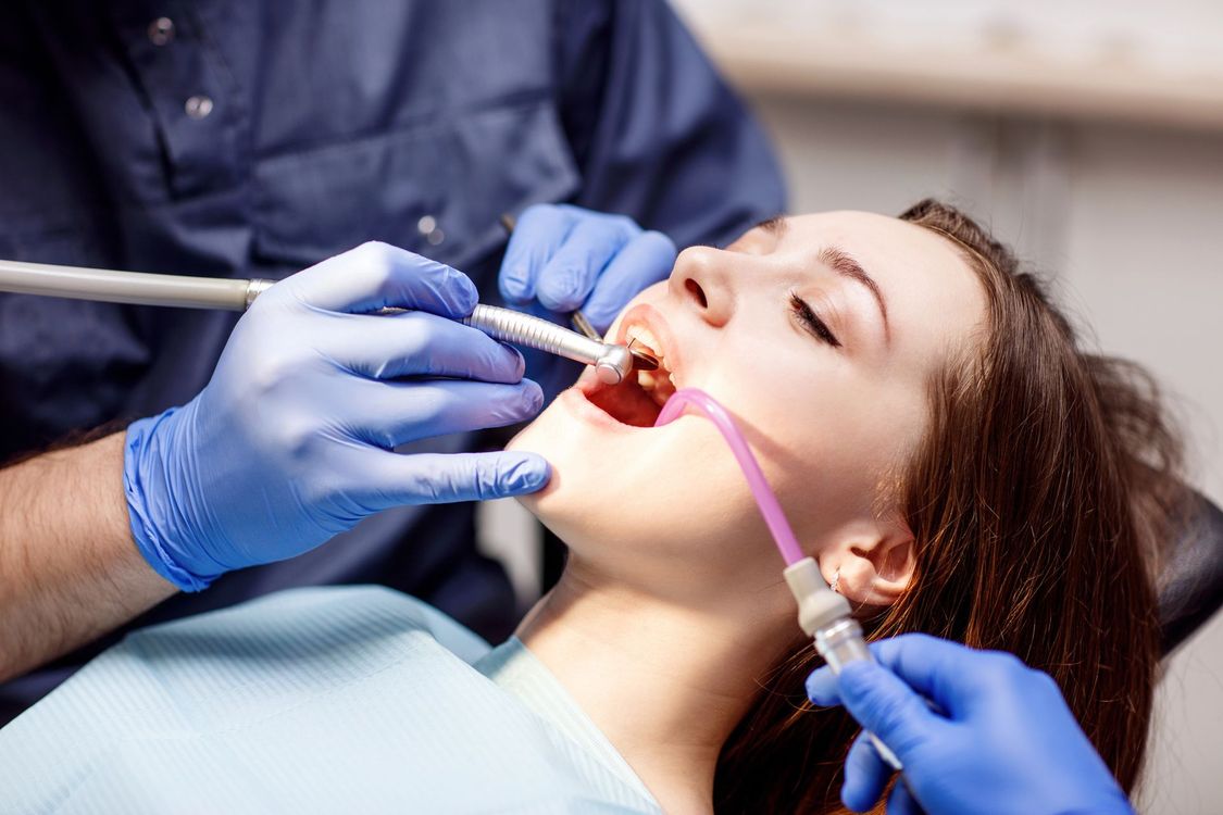 Dentista che cura la bocca aperta di un paziente con strumenti odontoiatrici e tubo di aspirazione.