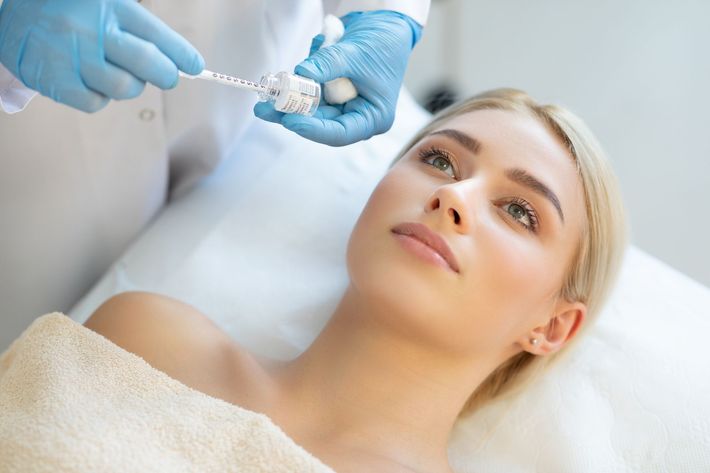 Mani guantate iniettano una sostanza a una donna sdraiata su un lettino da trattamento in una luminosa stanza della clinica.