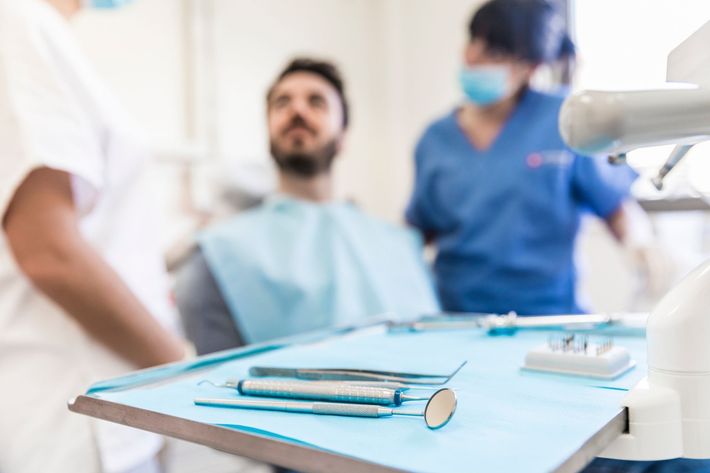 Strumenti odontoiatrici su un vassoio in una clinica, con un paziente e il personale con la mascherina sullo sfondo.