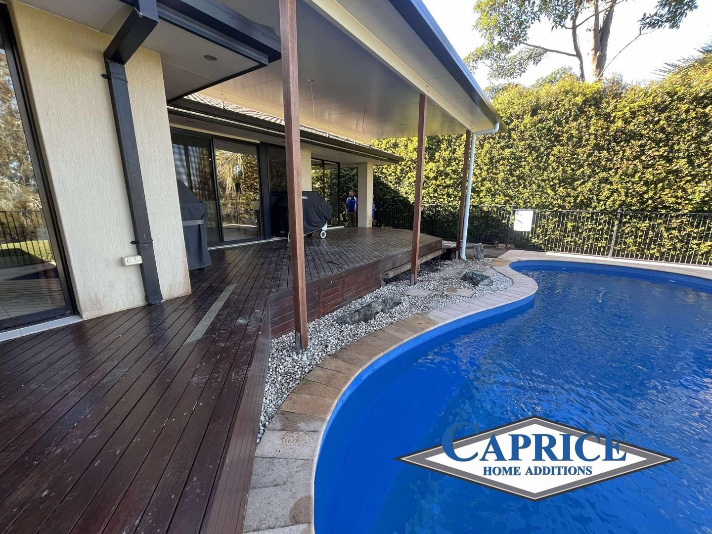 Covered Patio With Wood Decking Beside Curved Pool