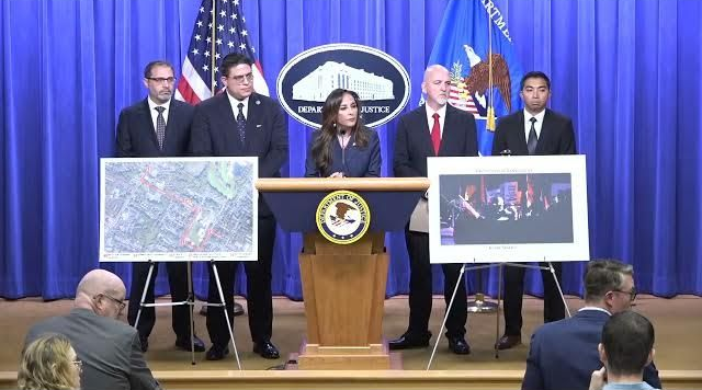 Press conference with officials behind a podium, diagrams and a photo on display.