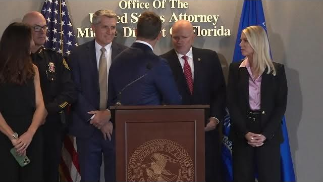 Group of people at a podium in front of a banner for the U.S. Attorney's Office, Florida.