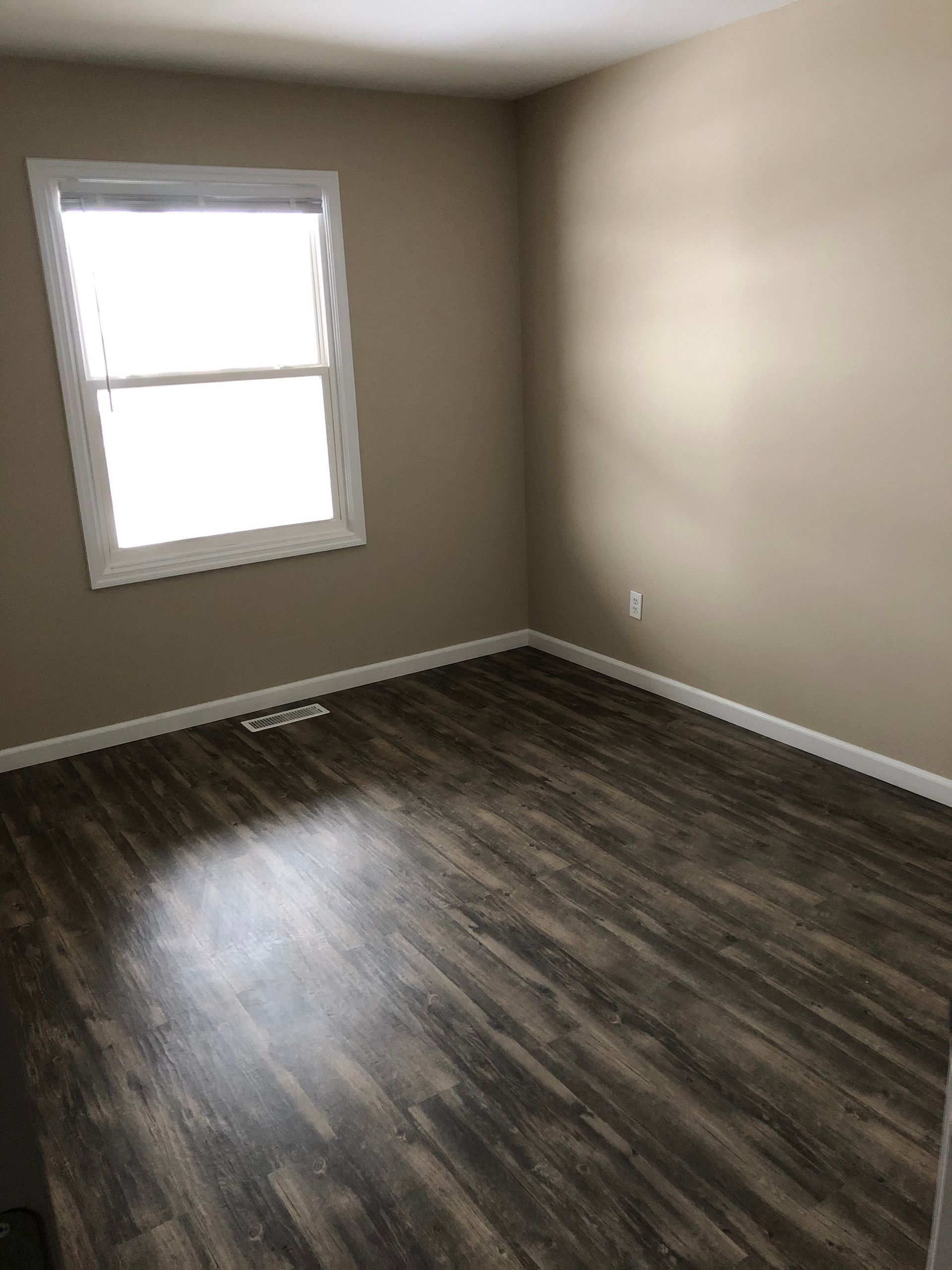Empty beige room with a window and dark wood flooring.