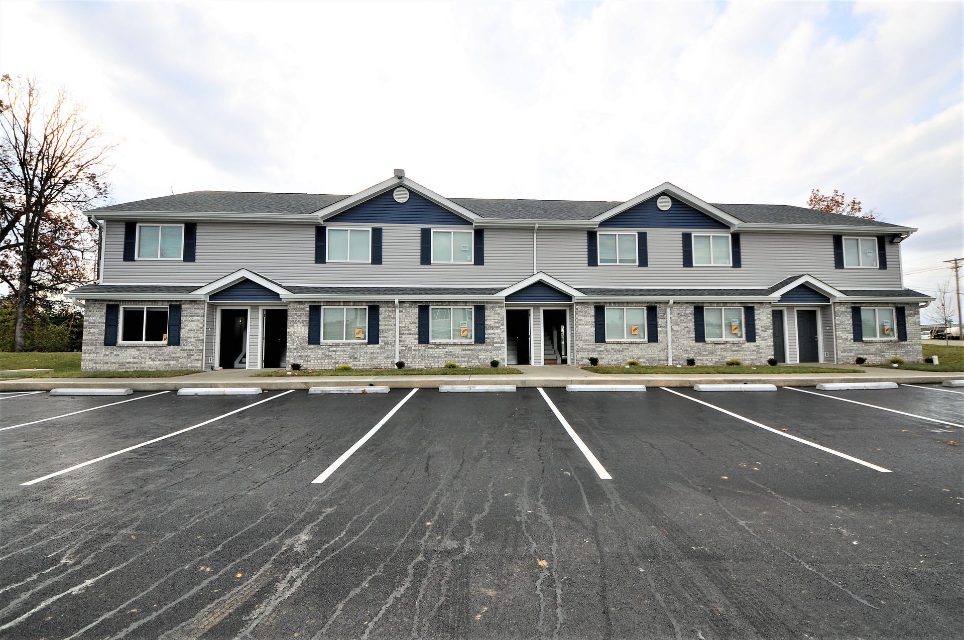 Two-story gray apartment building with empty parking lot in front